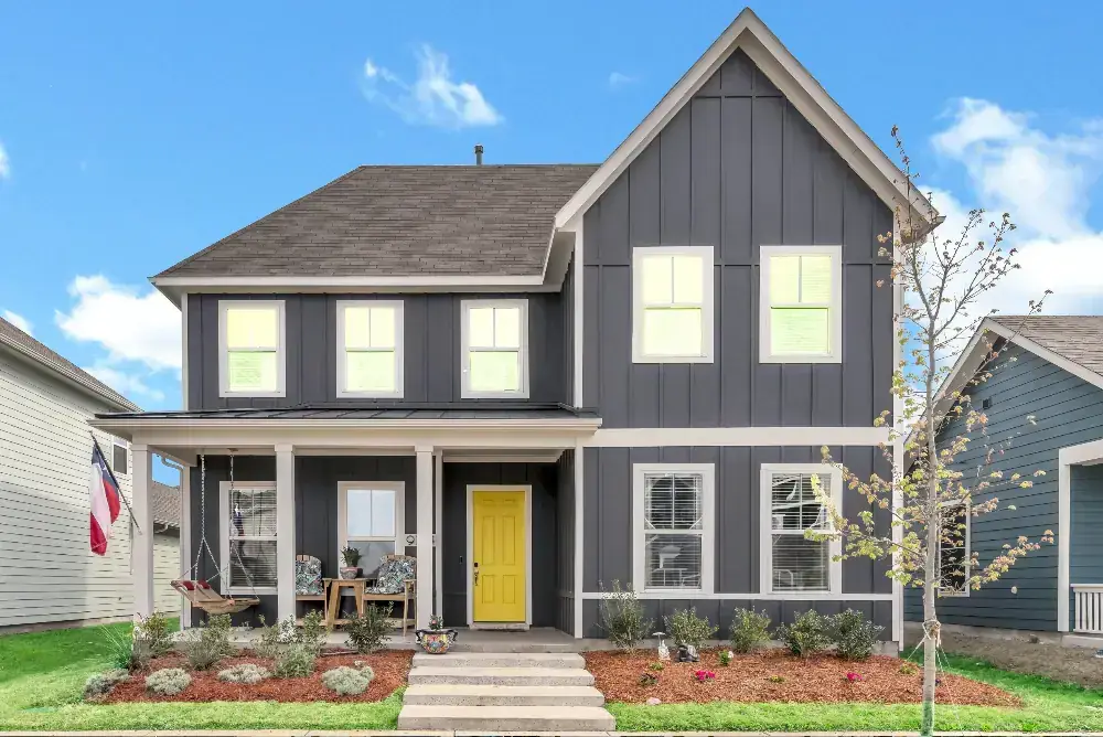 Real estate image of a two-story house with gray siding and a vibrant yellow door, highlighting its charming exterior.